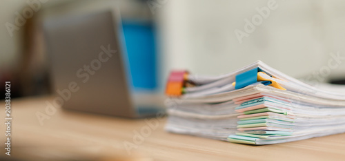 Stack of document files  paperwork  and reports organized with binder clips on a desk next to a blurred laptop  representing business management and data organization