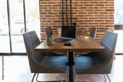 Modern workspace with laptop and chairs near brick wall indoors. Office interior with wooden table and business equipment. Business and remote work concept. Selective focus.
