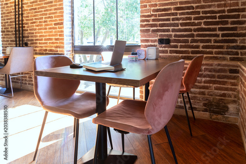 Modern office workspace with laptop and chairs near large window. Business interior with brick walls and indoor lighting. Productivity and corporate lifestyle concept. Selective focus.
