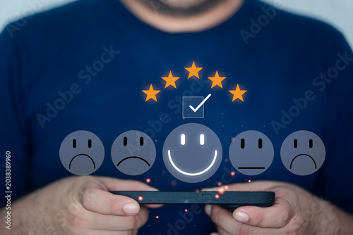 Customer Satisfaction Survey. Man engaged in completing a survey on a mobile phone, showcasing the options for satisfaction level. Pressing face emoticon smile in satisfaction on virtual screen.