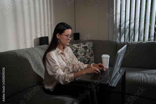 Woman with mug working on laptop in home living room creating comfortable remote work atmosphere and cozy home office lifestyle