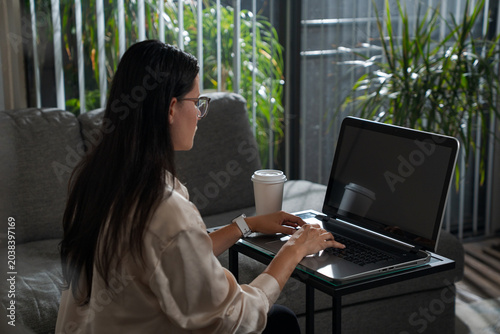 Young Woman Typing On Laptop Near Window At Home working remotely and maintaining productivity in a comfortable domestic environment