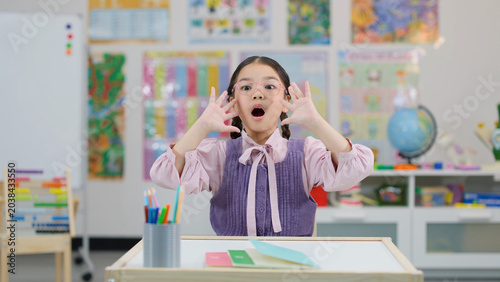 Принти на полотні Young Asian schoolgirl reacting with shock and amazement at a classroom desk