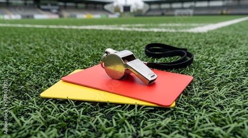 Professional referee equipment featuring a silver whistle resting on vibrant red and yellow penalty cards over a textured dark surface, symbolising fair play, rules, and sports officiating.