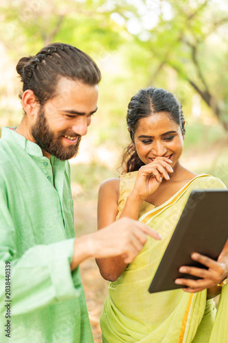 Indian couple watching funny videos on tablet outdoors