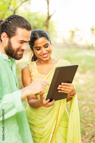 Indian couple watching funny videos on tablet outdoors