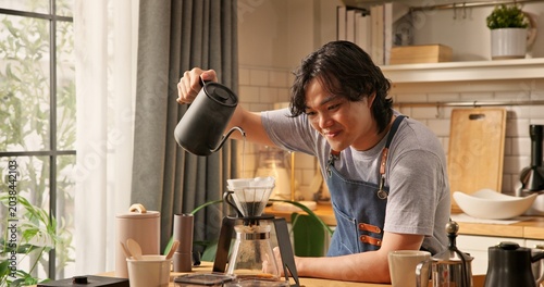 Fotografía Young Asian man pouring hot water from kettle into glass dripper with paper filter