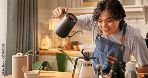 Foto Young Asian man pouring hot water from kettle into glass dripper with paper filter