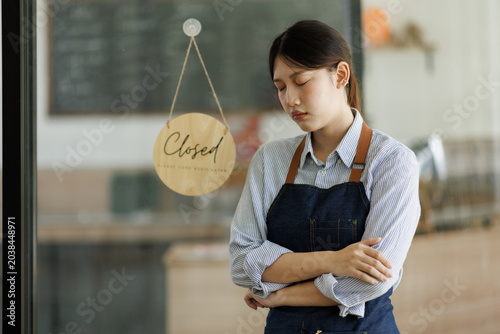 Fotografia Stressed small business owner standing by a closed sign, experiencing financial