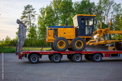 Road grader loaded on lowboy trailer for transport, heavy construction equipment. Concept: machinery logistics