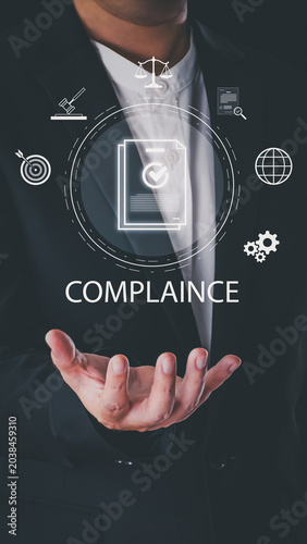 A businessman in a suit holds a virtual interface for compliance management. It features icons for law, ethics, and documents on a dark background during business hours.