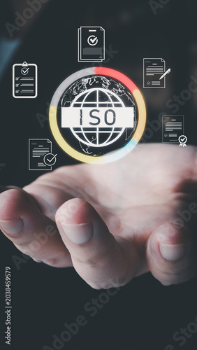 A hand holds a virtual ISO certification interface with a globe and document icons. It represents quality management and global standards for business on a dark background.