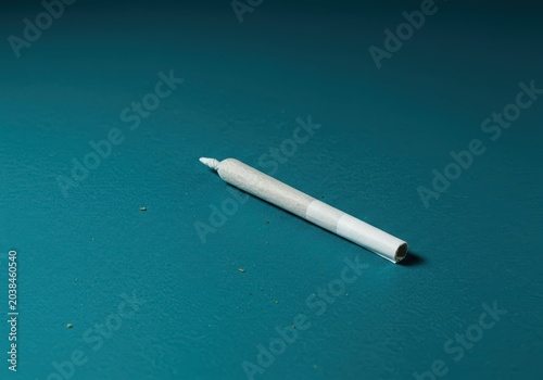 A single cannabis preroll joint resting on a vibrant, deep teal background, highlighting its preparation and ready-to-use form, cylindrical, aqua, background