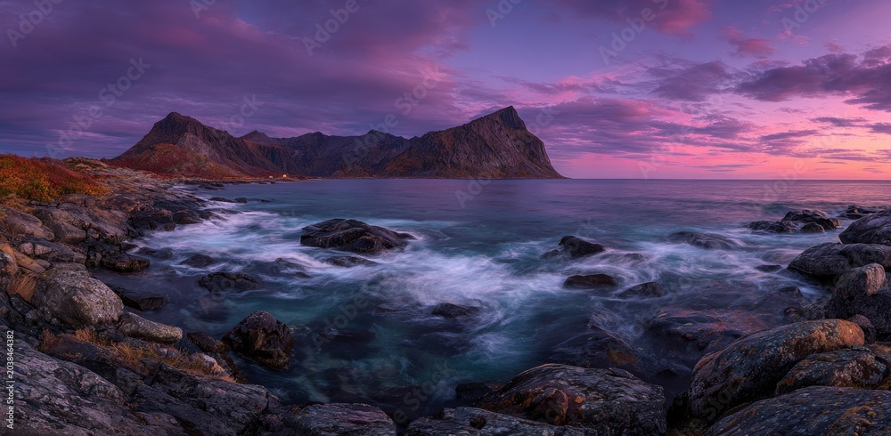 Obraz premium A coastal scene features mountains, ocean, and a striking sunset with a vibrant sky and rocky shore