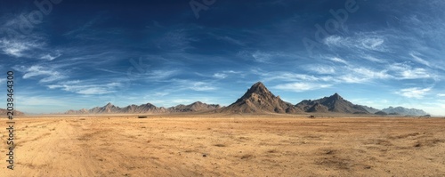 Vast panorama of a desert landscape under a vibrant, cloud-streaked blue sky, with distant mountains