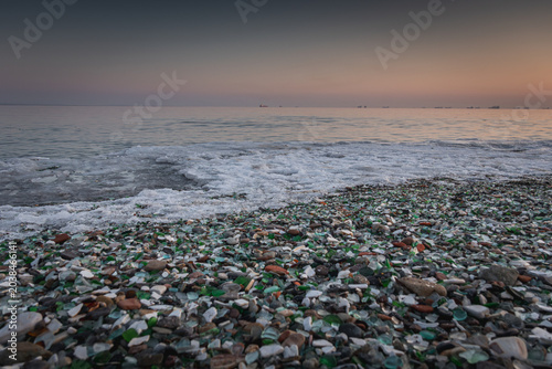 Obraz na plátně Shoreline covered with colorful sea glass and pebbles at sunset, gentle waves la
