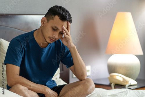 Stressed Asian Man Sitting on Bed with Headache