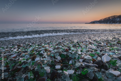 Obraz na plátně Colorful sea glass pieces scattered on a sandy beach at sunset, with gentle wave