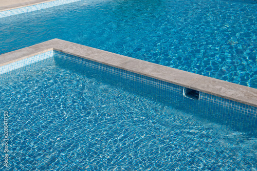 Foto Crystal clear blue swimming pool water with tiled edges and sunlight reflections