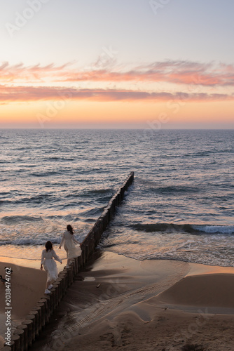 Two girls in white dresses walk along the breakwaters by the sea, view from above