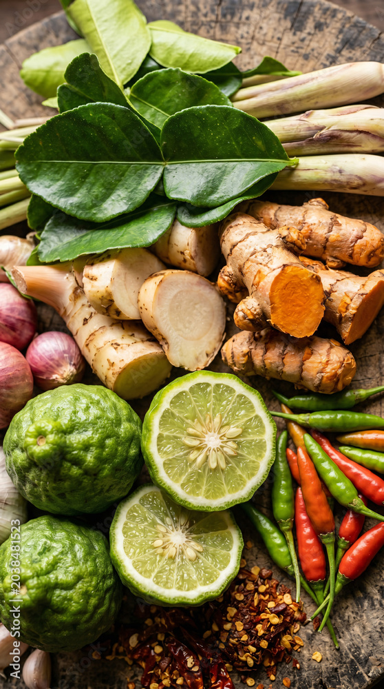 Fototapeta premium Fresh kaffir lime, turmeric root, lemongrass, chili peppers, shallots, and herbs on wooden board