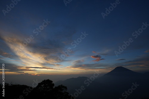 sunrise with mountain, trees, hills, shadows and morning fog