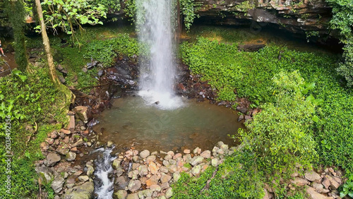 Schilderij op canvas Aerial View of a Waterfall Cascading into a Rocky Rainforest Pool