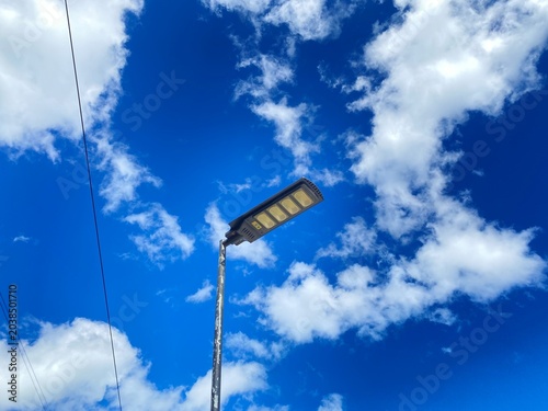 Solar street light outdoor with LED panel installed on pole under bright blue sky and clouds, renewable energy clean technology concept