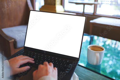 Mockup image of a woman working and typing on laptop computer with blank white desktop screen in cafe
