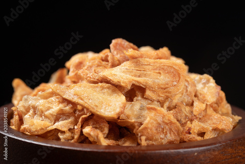 Crispy fried shallots in brown wooden bowl on a black background, crunchy Thai food