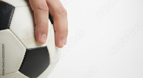 Close up of a hand holding a classic black and white soccer ball on a clean white background, emphasizing texture and detail