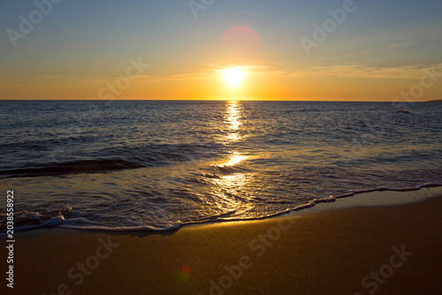 Golden sunset over the ocean with waves and colorful sky.