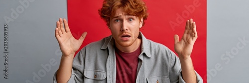 Shocked young man with raised hands and startled expression in front of red panel for wide banner or header design
