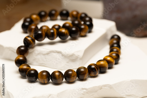 Tiger's eye stone is shaped into beads for jewelry. These beads are used in bracelets and necklaces. The jewelry is shown on a plain white surface.