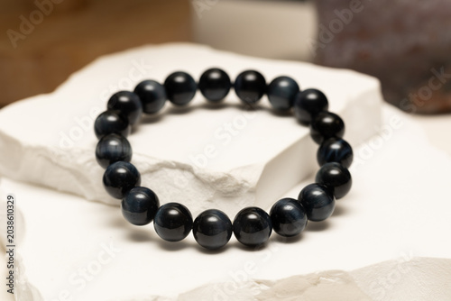 A blue tiger eye bracelet is placed on a white stone surface. The bracelet shows its round beads and displays its natural features.