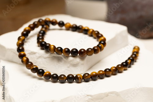 Tiger's eye stone is shaped into beads for jewelry. These beads are used in bracelets and necklaces. The jewelry is shown on a plain white surface.