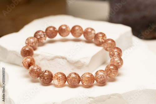 A Tangerine natural stone bracelet is displayed on a white stone surface. The bracelet has round beads that reflect light. The setting highlights the bracelet's unique texture.