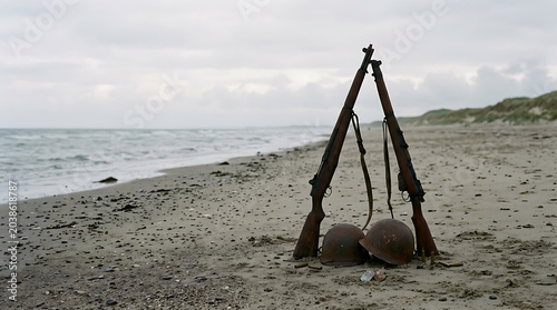 Poignant military rifles and helmets stand silently on a desolate beach, evoking remembrance and honoring the D-Day Anniversary sacrifices