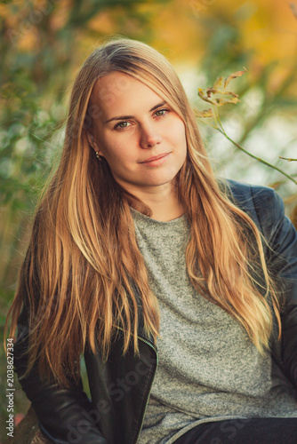Portrait of calm young woman with long blonde hair and green eyes outdoors in autumn