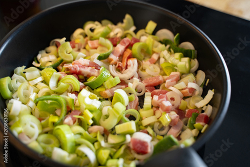 Closeup of frying pan with bacon and leek on the stove