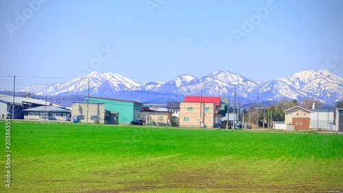 Scenic landscape of snow-capped mountains and green fields in Hokkaido, seen from a moving train window.