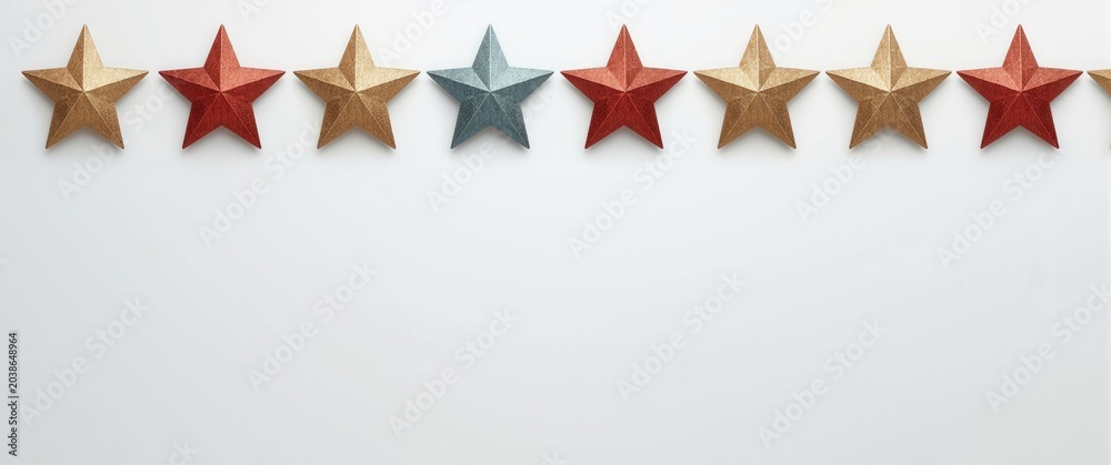 Fototapeta premium Decorative stars in gold blue and red arranged in a straight line on a white background with copy space