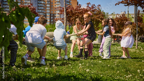Tableau sur toile Group of children pulling rope in tug of war game on green grass
