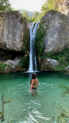 Фотография Person swimming in a natural pond beneath a waterfall, summer nature scene