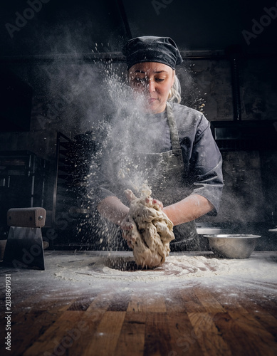 Female baker kneading dough with flour explosion in bakery kitchen