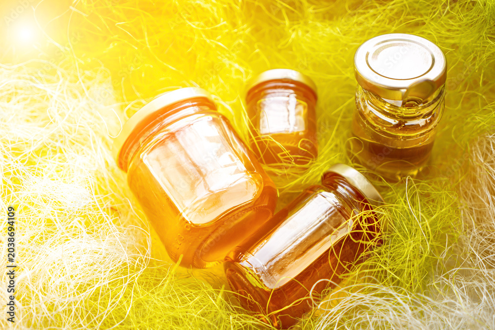 Fototapeta premium Honey in glass jars with flowers background.