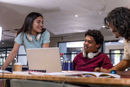 Diverse students studying together at communal table with silver laptop, headphones, coffee cup