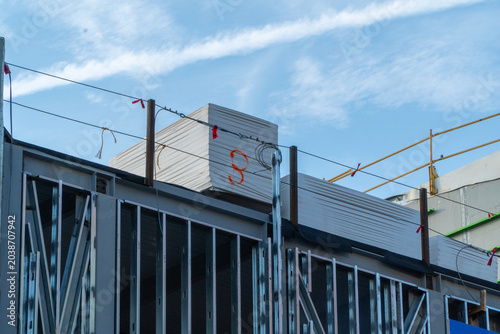 Fotografie Building under construction with metal framing and stacked insulation panels against a bright blue sky, showcasing urban development and ongoing work in the construction industry