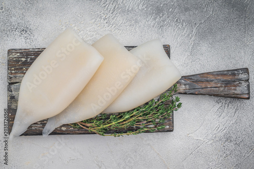 Raw calamari arranged with herbs on weathered wood against a gray stone backdrop ideal for culinary seafood stock concepts.