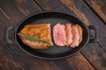 Seared duck breast sliced and served in cast-iron skillet with thyme on rustic wooden background ideal for gourmet food photography.